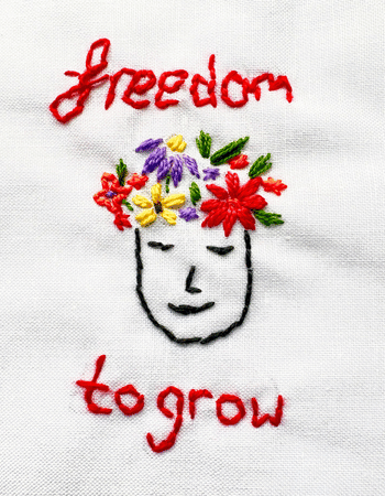 Threads of Freedom Stitching onto white cloth with the words 'freedom to grow' with an image of a face with flowers on the head.