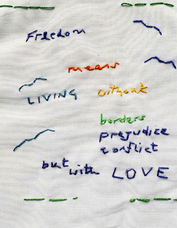 Threads of Freedom stitching on white cloth with the words 'Freedom means living without borders, prejudice, conflict but with love' in different colours